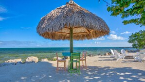 A beach with a thatched umbrella, wooden chairs, and a view of the ocean. - Overlooking Pool Free Golf Cart Free Kayaks Pickleball (Key Largo)