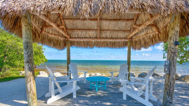 A beachside gazebo with a thatched roof, white Adirondack chairs, and a turquoise table. - Overlooking Pool Free Golf Cart Free Kayaks Pickleball (Key Largo)