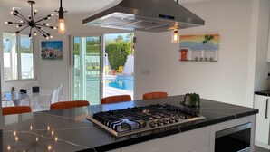 Een moderne keuken met een centraal eiland, roestvrijstalen apparatuur en een groot raam met uitzicht op een zwembad.