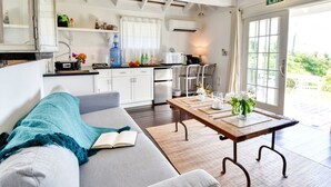 A cozy living room with a sofa, a wooden table, and a view of the garden through a glass door. - 1BR Hillside Cottage on Peaceful Private Estate (Governor's Harbour)