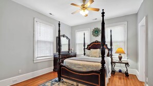 Quarto com cama de dossel, ventoinha no teto e piso de madeira.