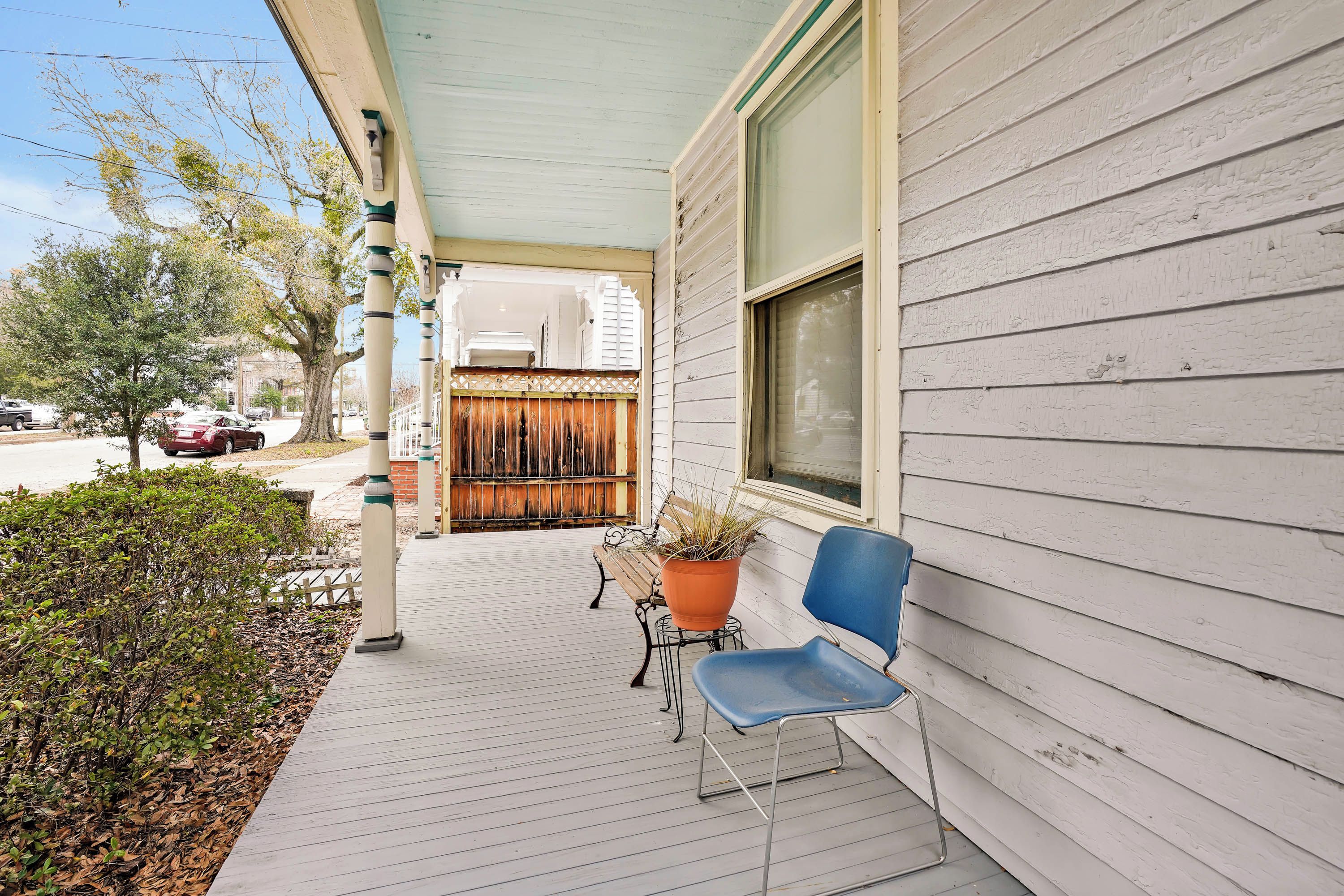A covered porch with a bench and a potted plant, a wooden fence, and a street view.