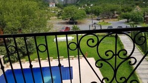 Vista desde un balcón con piscina, que da a un valle con acantilados rocosos, vegetación y una carretera con coches estacionados.