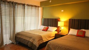 Una habitación de hotel con dos camas, una mesita de noche con lámpara y una cortina.