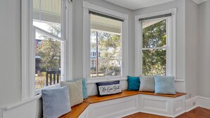 A room with a built-in bench under large windows, a decorative pillow with text, and a view of the outside. - Savannah Suite on Front (Wilmington)