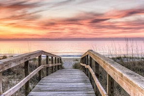 A wooden boardwalk leading to the beach with a sunset in the background. - Savannah Suite on Front (Wilmington)