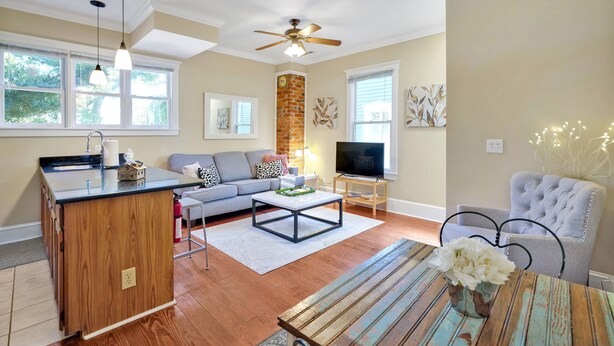 A modern living room with hardwood flooring, a kitchen island, a grey sofa, a television, and a ceiling fan. - Condo Riviere Stay Downtown! Walk everywhere! (Wilmington)