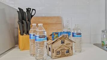 Un comptoir de cuisine avec des bouteilles d’eau de la marque Kirkland, une maquette de maison en bois et un bloc à couteaux.