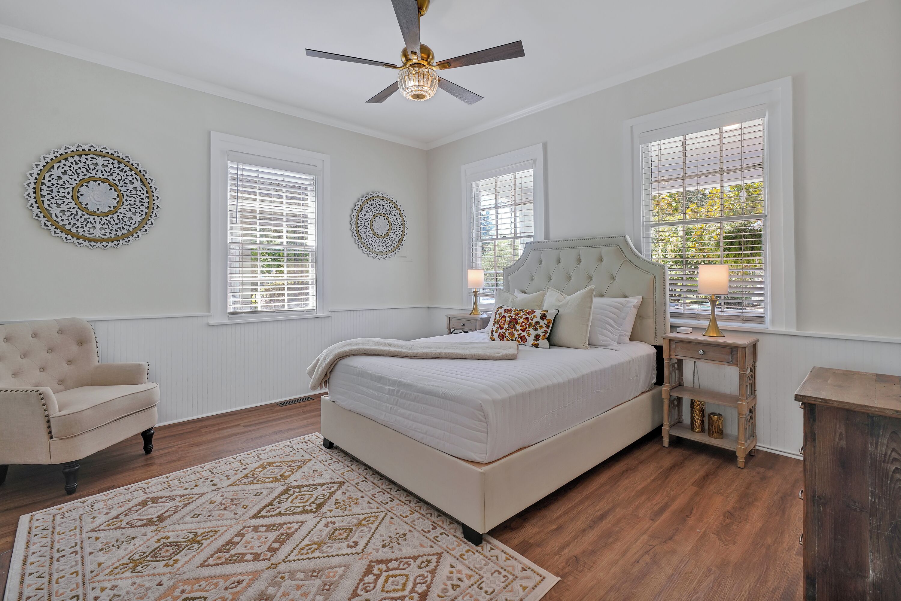 A bedroom with a large bed, a chair, a nightstand, and a ceiling fan.
