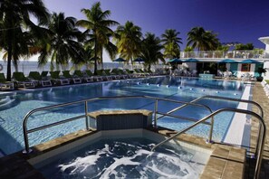Een zwembad met een jacuzzi, omgeven door palmbomen en ligbedden.