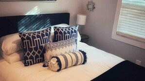 A neatly made bed with patterned pillows, a decorative wall piece, and a lamp.