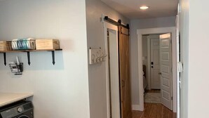 A laundry area with a washing machine, a trash can, and a wooden shelf with items.