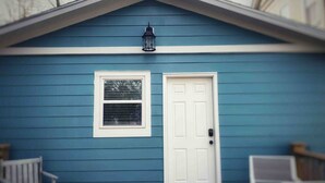 A blue house with a white door and window, a porch with two chairs, and a lantern above the door.