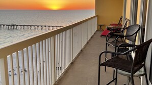 Un balcón con vista al océano al atardecer, que incluye barandilla, una mesa y dos sillas.