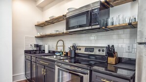 Een moderne keuken met roestvrijstalen apparatuur, houten planken en een zwart aanrecht.