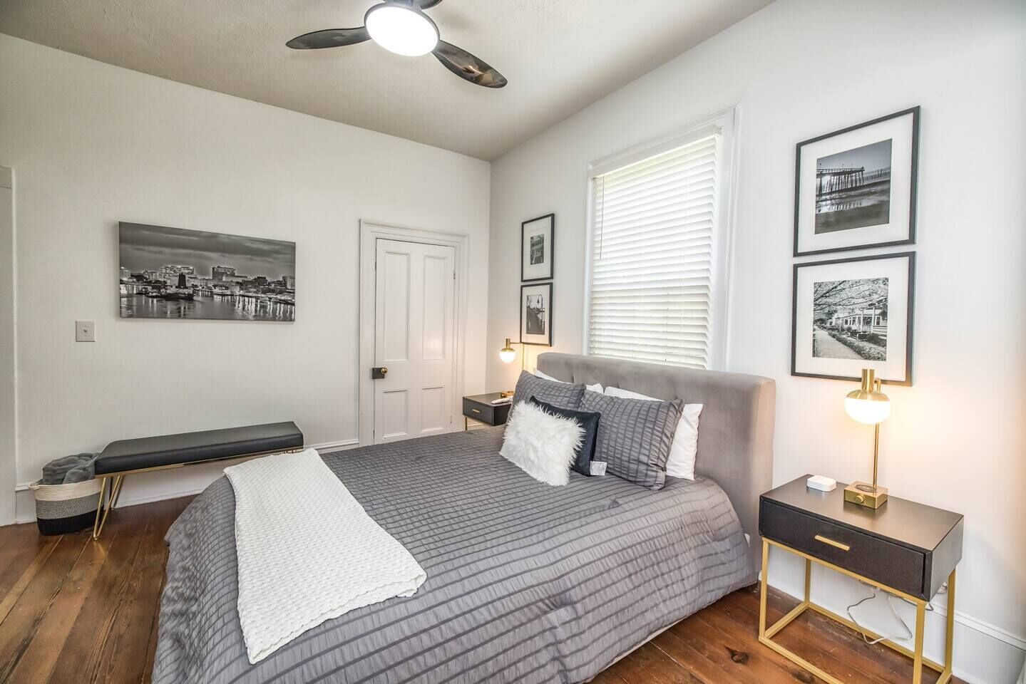 A bedroom with a bed, bedside tables, a bench, and framed pictures on the wall.