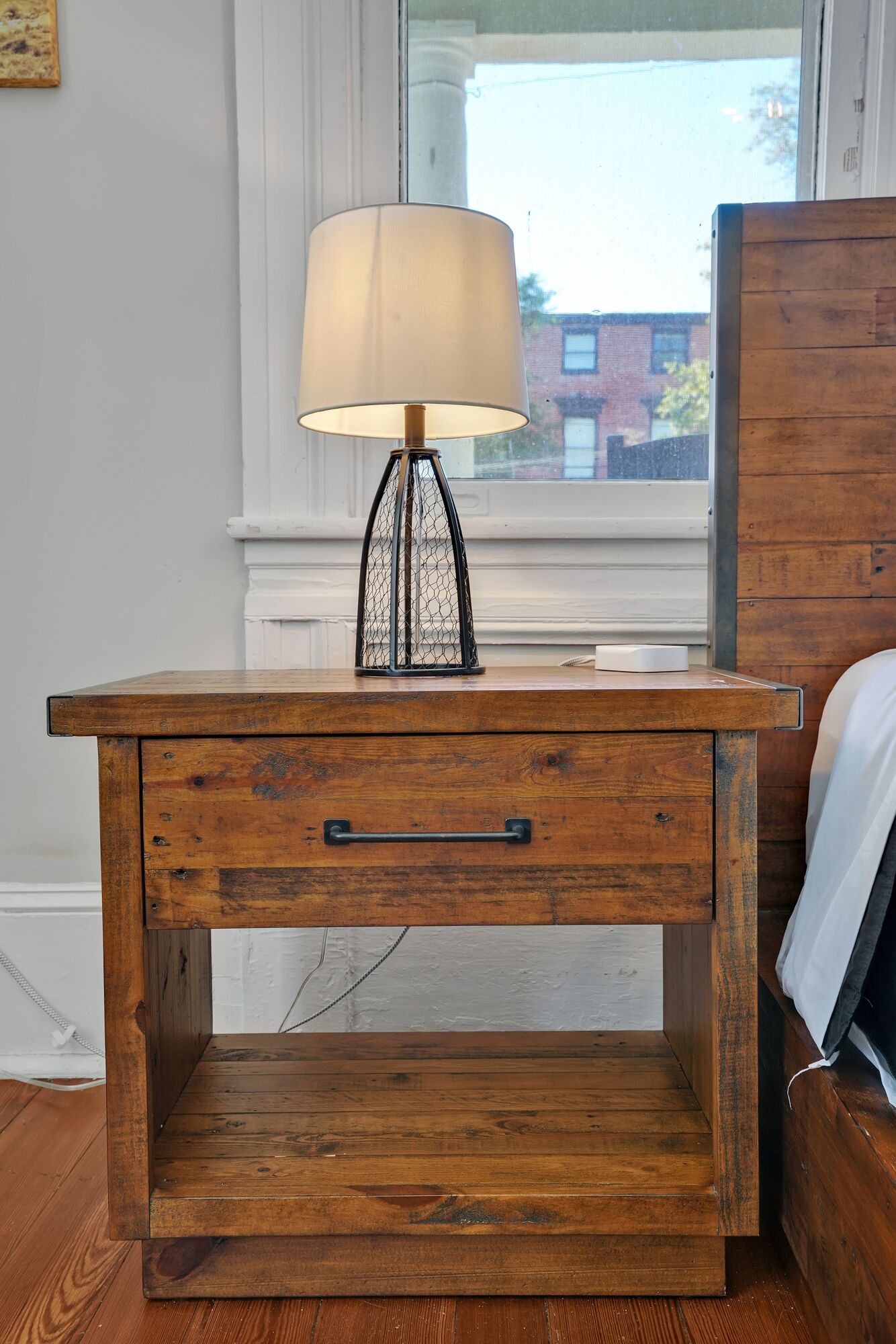 A wooden bedside table with a lamp, a drawer, and a shelf.