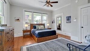 Une chambre à coucher avec un lit en bois, un ventilateur de plafond et de grandes fenêtres.