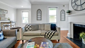 Un salon comprenant un canapé, des fauteuils, une table basse avec des livres, une cheminée et une grande horloge murale.