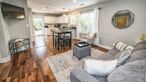 A spacious living room with a gray sofa, a coffee table, and a dining area with a kitchen in the background. - The Relaxing Zen Garden. You've found it. (Wilmington)