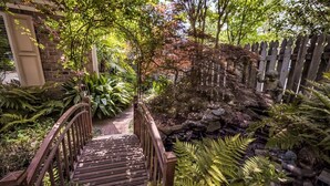 A wooden bridge leading to a garden with a stone wall and ferns. - The Relaxing Zen Garden. You've found it. (Wilmington)