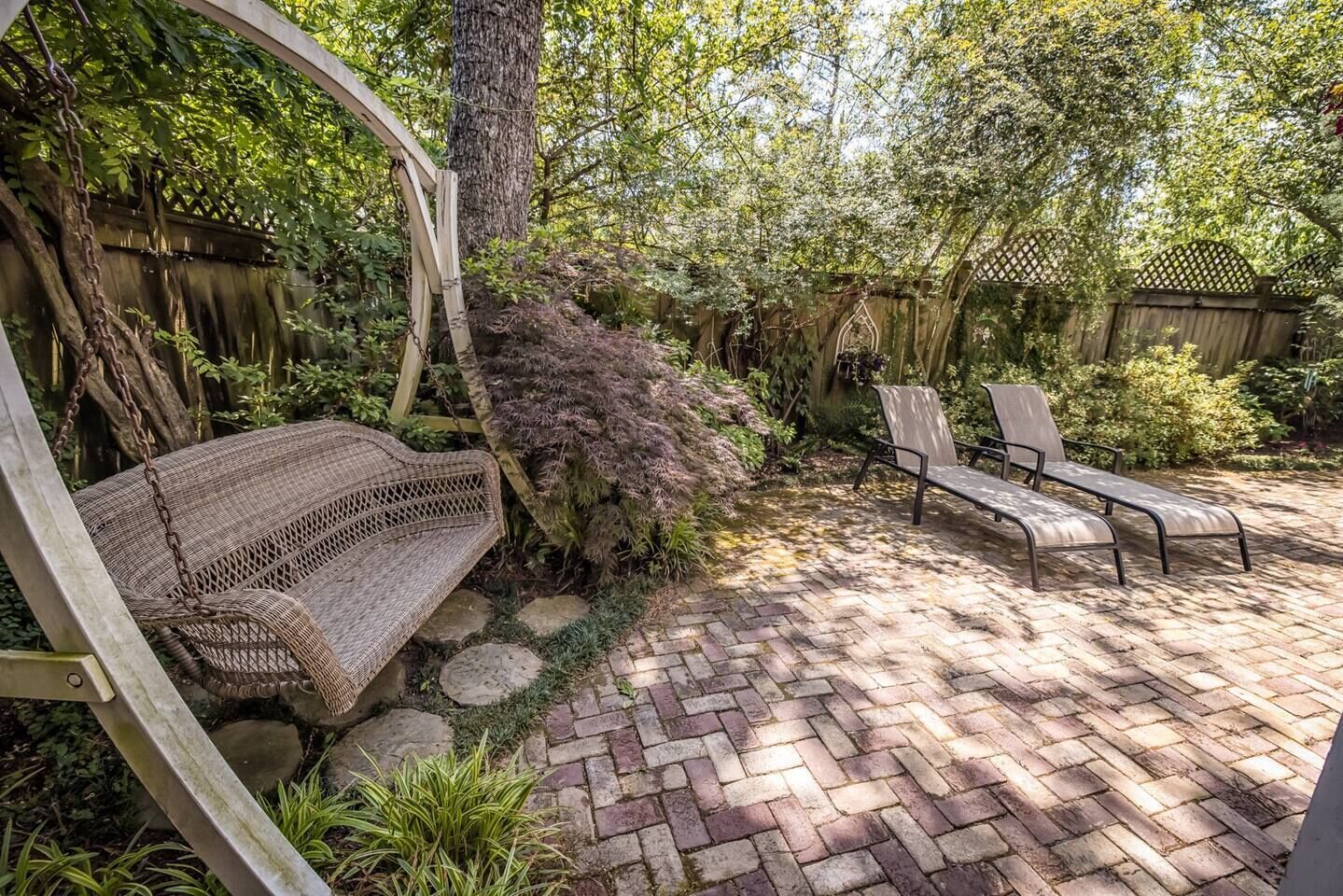 A patio with a wicker swing, two lounge chairs, and a brick pathway.