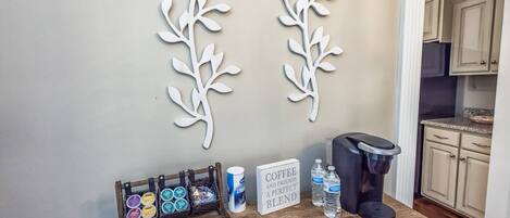 A kitchen area with a coffee station, including a coffee maker, cups, and a sign that reads "Coffee and Friends a Perfect Blend".
