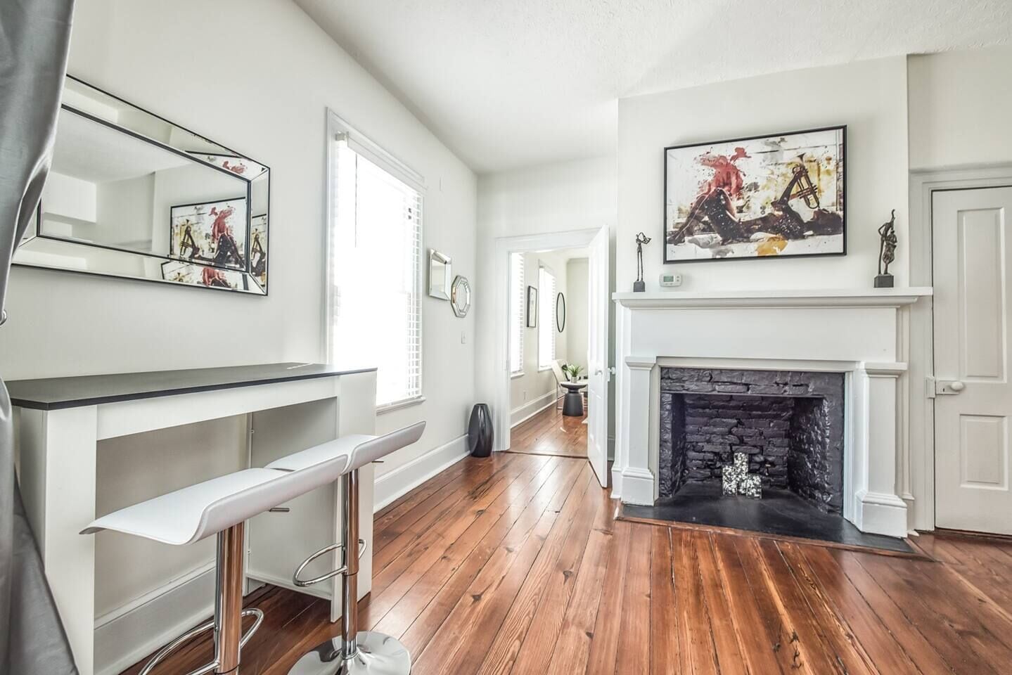 A spacious room with a wooden floor, a white fireplace, and a large mirror on the wall.
