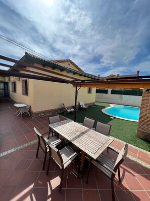 Eine Terrasse mit Tisch und Stühlen, ein Pool und ein überdachter Bereich mit einer Pergola.