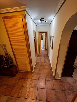 Ein Flur mit Holztüren und Fliesenboden, der zu einem Badezimmer mit Schachbrettmuster auf dem Boden führt.