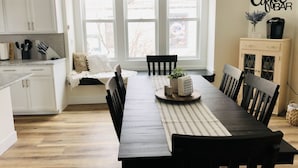 Una cocina moderna con armarios blancos, una mesa de comedor con sillas y un ventanal con persianas.