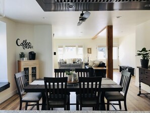 A dining area with a table and chairs, a coffee bar sign on the wall, and a view into a living room with a sofa and a lamp. - Luxury on Main, remodeled, homey, fresh and bright! (Bozeman)