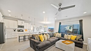 A modern living room with a sectional sofa, a coffee table, and a dining area with a kitchen in the background. - The Legacy Retreat Near National Parks! (Hurricane)