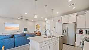 A modern kitchen with white cabinetry, a built-in dishwasher, a stainless steel refrigerator, and a large island with a sink. - The Legacy Retreat Near National Parks! (Hurricane)