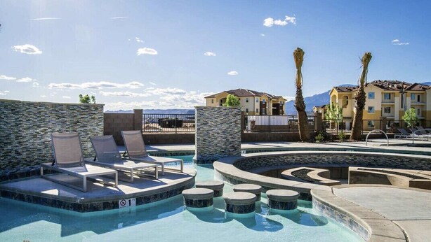 A pool area with lounge chairs, a stone wall, and a view of buildings in the background. - The Legacy Retreat Near National Parks! (Hurricane)