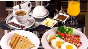 A breakfast setting with a cup of coffee, a glass of orange juice, toast, eggs, bacon, and a small bowl of butter. - Galo Vela (Santo Domingo de los Colorados)