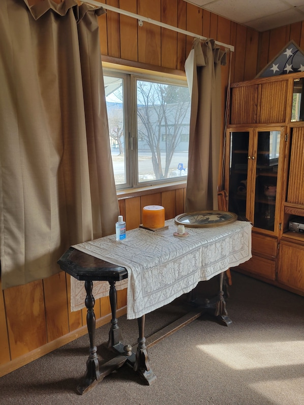 A room with wooden walls, a table with a lace tablecloth, a candle, and a window with curtains. - Private home in beautiful Northeast Washington (Ione)