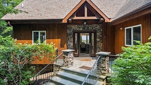 A wooden cabin with a stone entrance, a covered porch, and a staircase leading to the door. - NEWLY RENOVATED! Lake George Mtn Retreat: Hot tub, BBQ, Firepit, 2-tiered Deck! (Lake George)