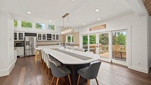A modern kitchen with a large island, built-in appliances, and a sliding glass door leading to an outdoor patio. - NEWLY RENOVATED! Lake George Mtn Retreat: Hot tub, BBQ, Firepit, 2-tiered Deck! (Lake George)