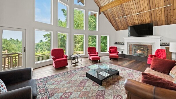A spacious living room with large windows, a fireplace, and red furniture. - NEWLY RENOVATED! Lake George Mtn Retreat: Hot tub, BBQ, Firepit, 2-tiered Deck! (Lake George)