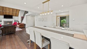 A spacious living area with a fireplace, a long dining table, and a modern chandelier. - NEWLY RENOVATED! Lake George Mtn Retreat: Hot tub, BBQ, Firepit, 2-tiered Deck! (Lake George)