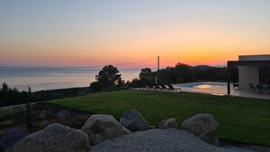 Ein Sonnenuntergang über einem Pool mit einer Rasenfläche und Felsen im Vordergrund.