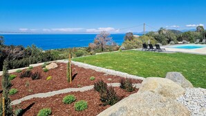 Ein Poolbereich mit Liegestühlen, freier Meerblick und ein angelegter Garten mit Mulch und Steinen.