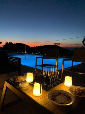 Un espace de restauration en plein air avec vue sur la piscine, des tables décorées de bougies et des plats de nourriture.