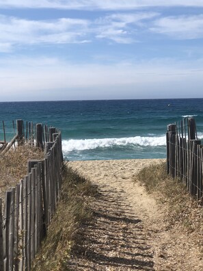 A sandy beach path leading to the ocean, bordered by wooden fences.