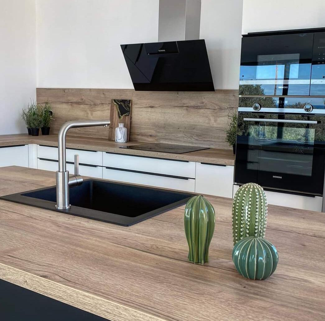 A modern kitchen with a black sink, stainless steel faucet, wooden countertop, and a built-in oven.