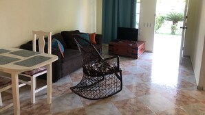 A living room with a sofa, a TV on a wooden cabinet, a dining table with chairs, and a ceiling fan.