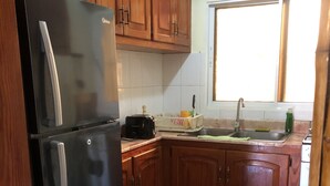 A kitchen with wooden cabinets, a black refrigerator, a sink, and a window.