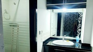 Une salle de bain moderne avec une douche à l’italienne en verre, un lavabo blanc et des meubles de couleur sombre.