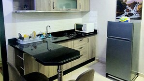 Une cuisine compacte dotée d’un plan de travail noir, de meubles en bois, d’un four à micro-ondes, d’un réfrigérateur et d’un coin repas avec deux chaises.